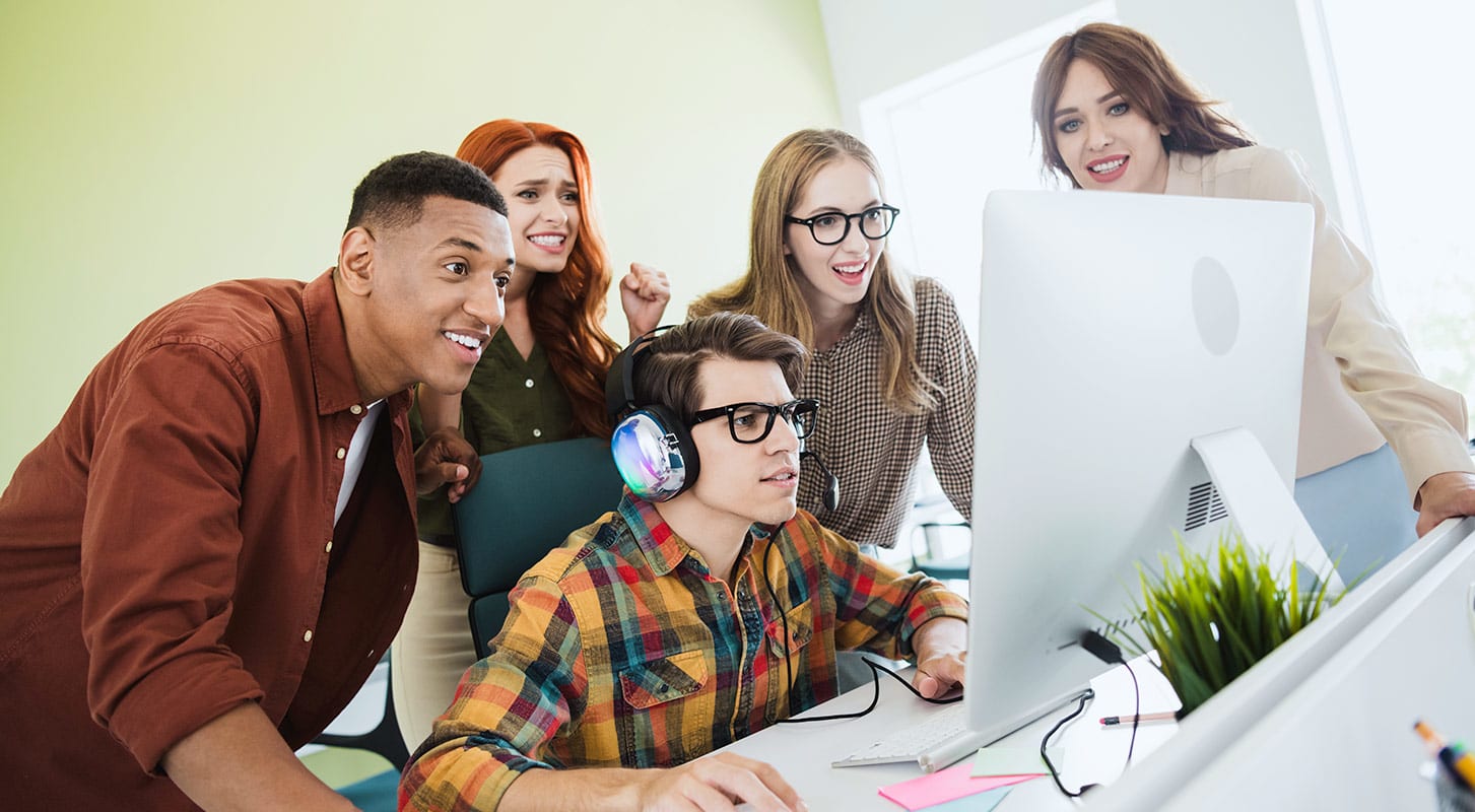 A group of people gathered around a computer screen, engaged in discussion and looking at the displayed content.